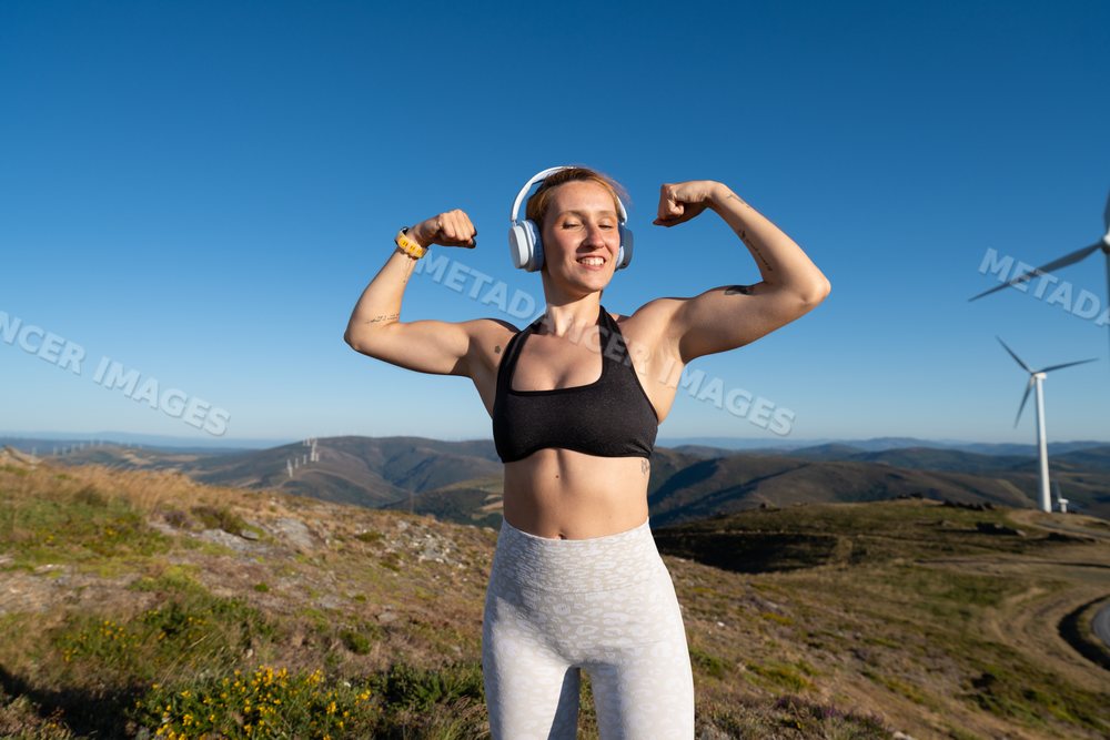 A fit white woman flexing muscles outdoors with wind turbines
