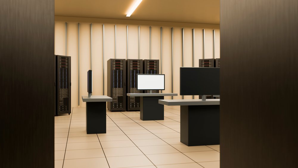Server racks and computer monitors arranged in a clean, modern data center room with tiled floor and vertical wall lights.