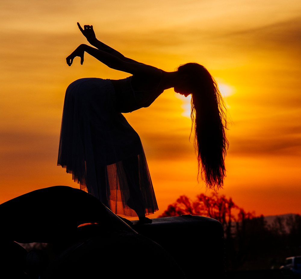 Silhouette of a female dancer in a ballet skirt posing gracefully outdoors at sunset with an orange sky, USA.