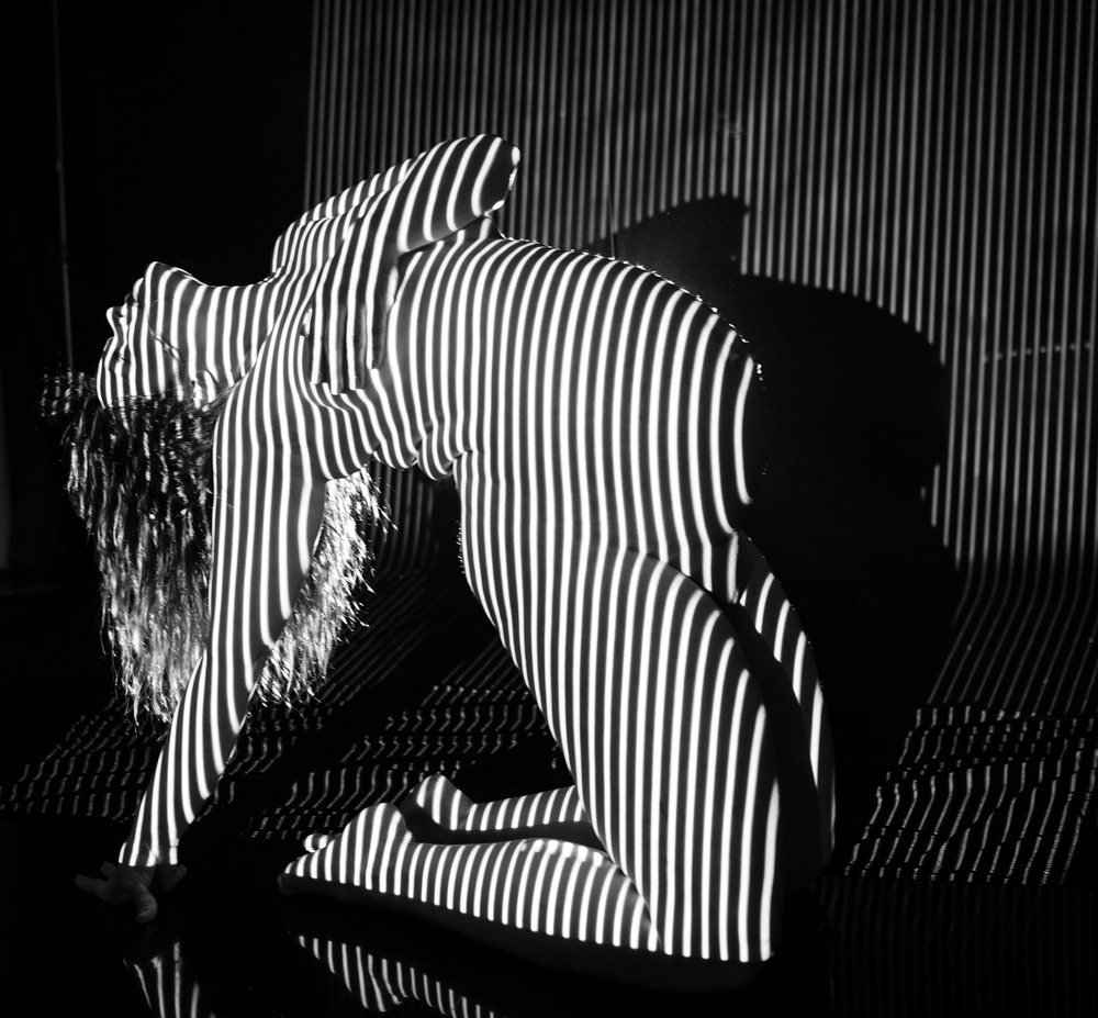 Pregnant woman kneeling and bending backward under black and white striped light projection in studio, pregnancy.