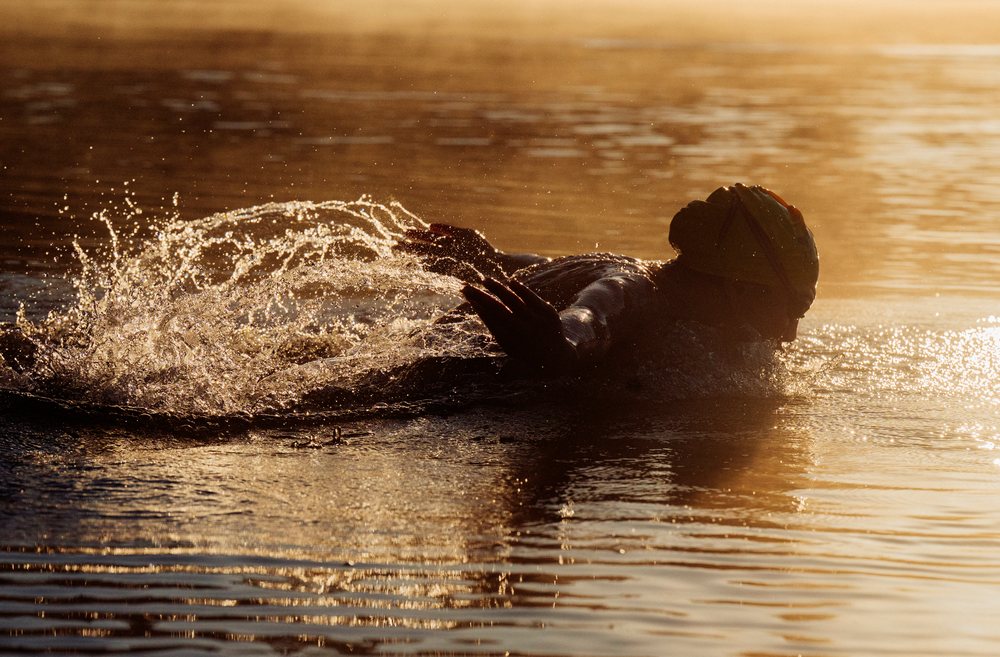 Swimmer wearing a swimming cap performing the backstroke in open water at sunset, USA.
