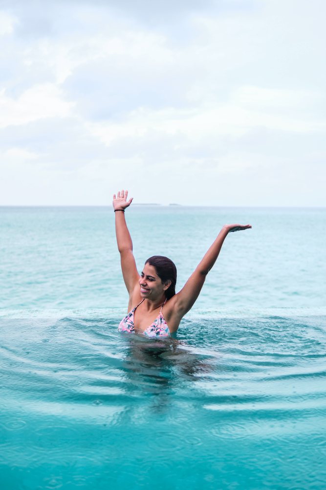 A white woman raises her arms swimming in an infinity pool