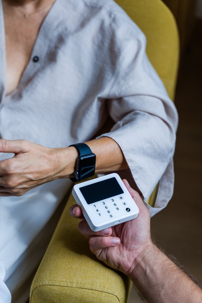 Person using a smartwatch to make a contactless payment on a white terminal indoors, Spain.