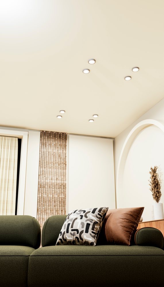 Green upholstered sofa with patterned and brown pillows in a modern living room with wood paneling, arch detail, and recessed ceiling lights.