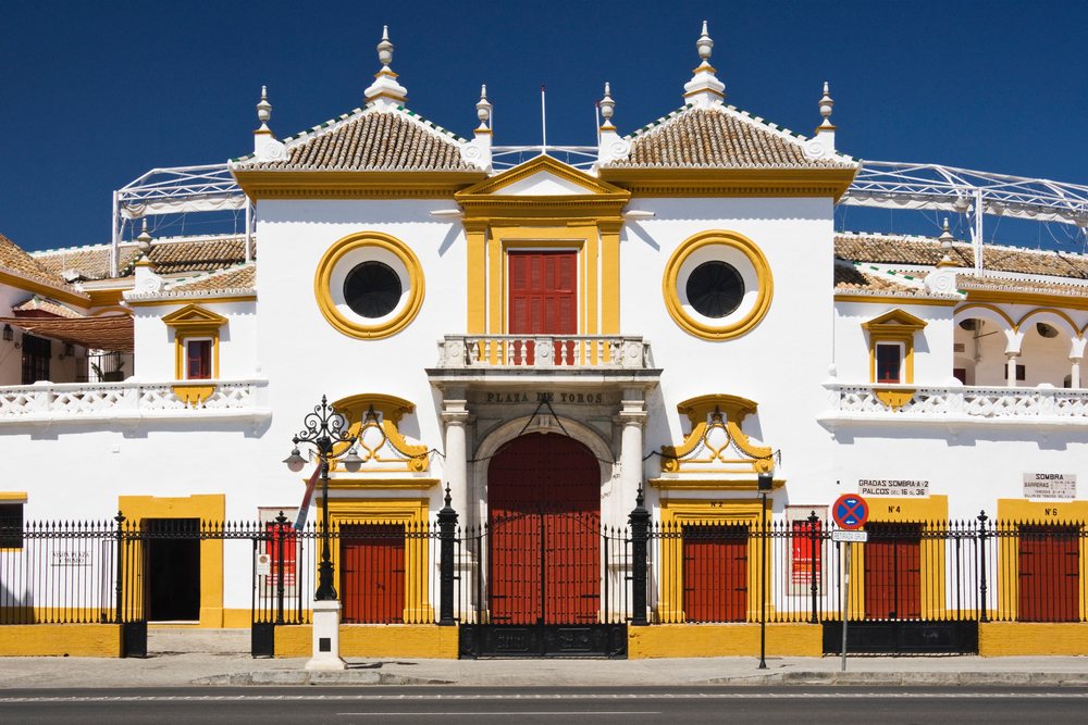 Historic Plaza de Toros de la Maestranza bullring with white and yellow facade and red gates, Andalucia, Spain.
