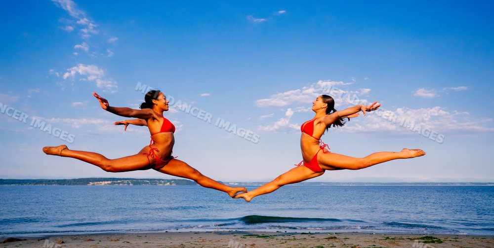 Two women performing a synchronized Yoga partner acrobatics leap