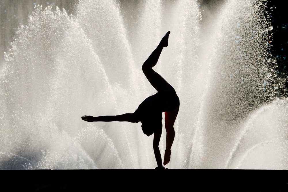 Silhouette of a person performing a handstand outdoors in front of a large water fountain, USA.