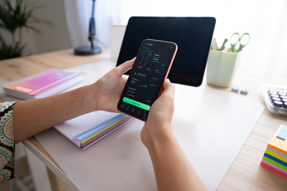 Person holding a smartphone with a charging app above a wooden desk, home, girl, Spain.