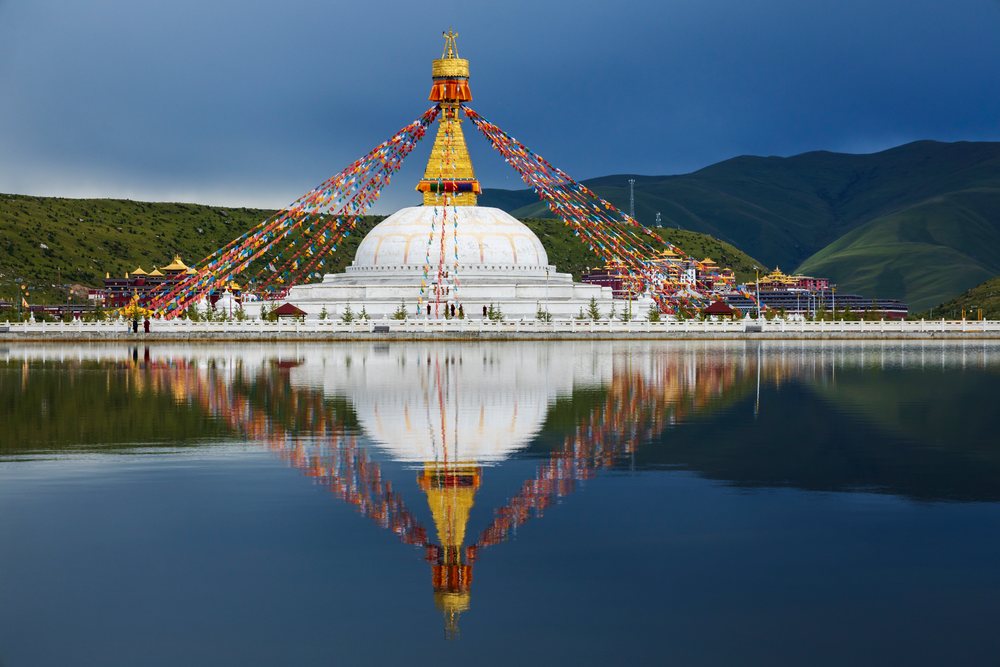 Large white stupa with golden spire at Zhuqing Wujian Zen Forest Monastery reflects clearly in lake amid green hills and mountains, China, Sichuan Province, People's Republic of China.