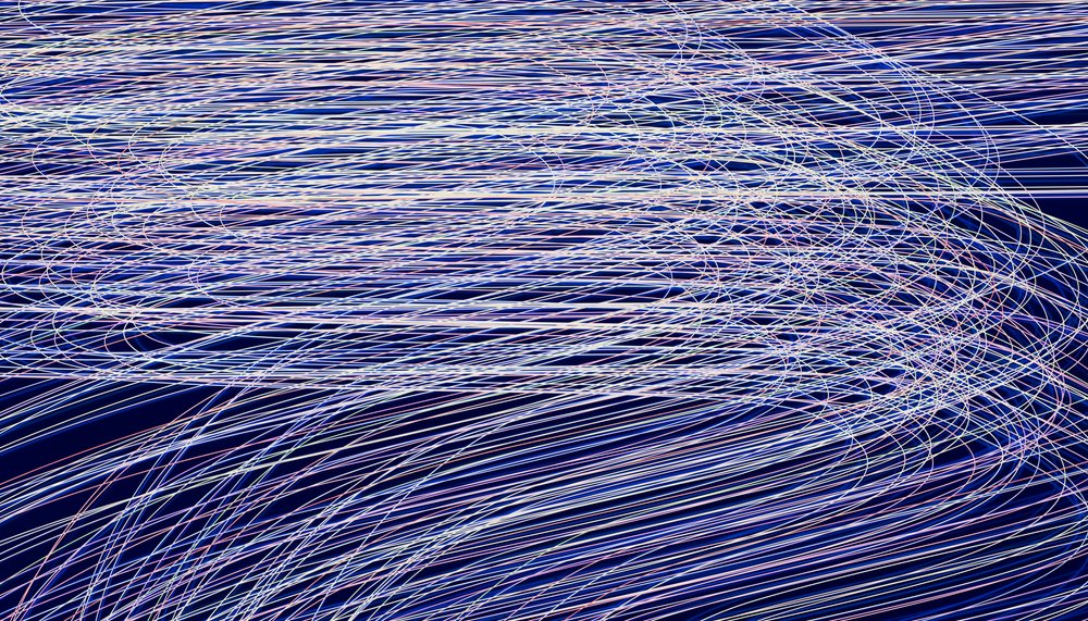 Light trails captured with long exposure create dynamic curved streaks of blue and white on a dark background forming an abstract visual pattern.