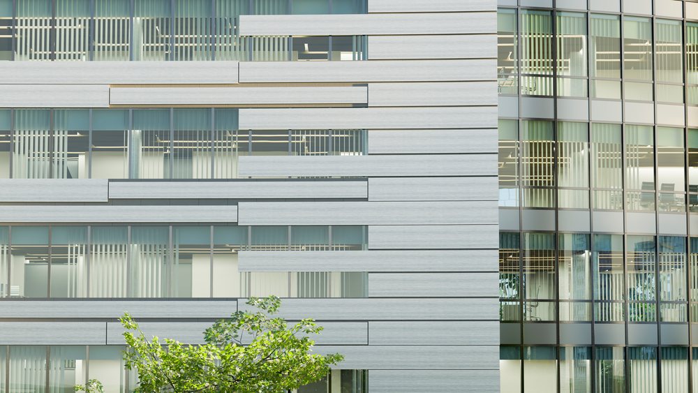 Modern office building exterior with glass windows and steel panels under daylight.