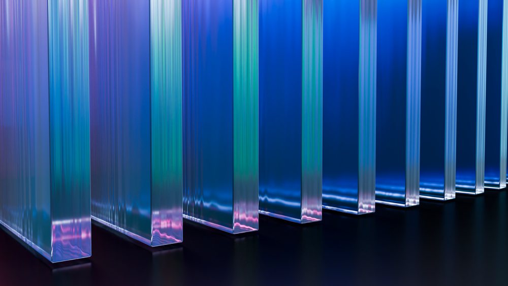 Vertical transparent glass panels reflect blue and purple hues with light refraction creating color gradients in a modern abstract design.