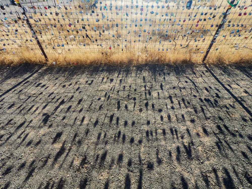 Love locks hang on a wire mesh fence casting shadows over gravel and dry grass at Prada Marfa, landscape, wildlife, Valentine, Texas, USA.