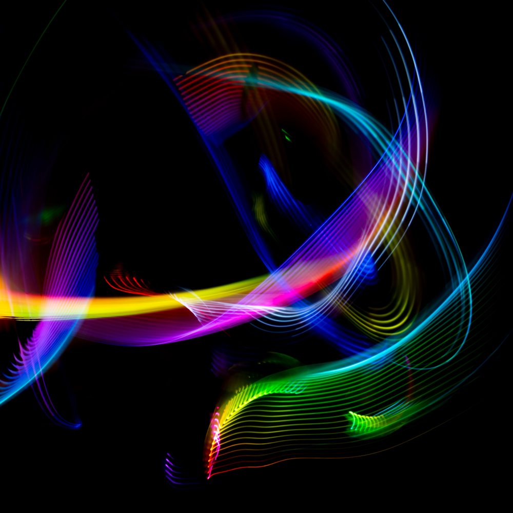 Colorful LED light trails in curved and swirling lines against a dark black background captured by long exposure light painting photography.