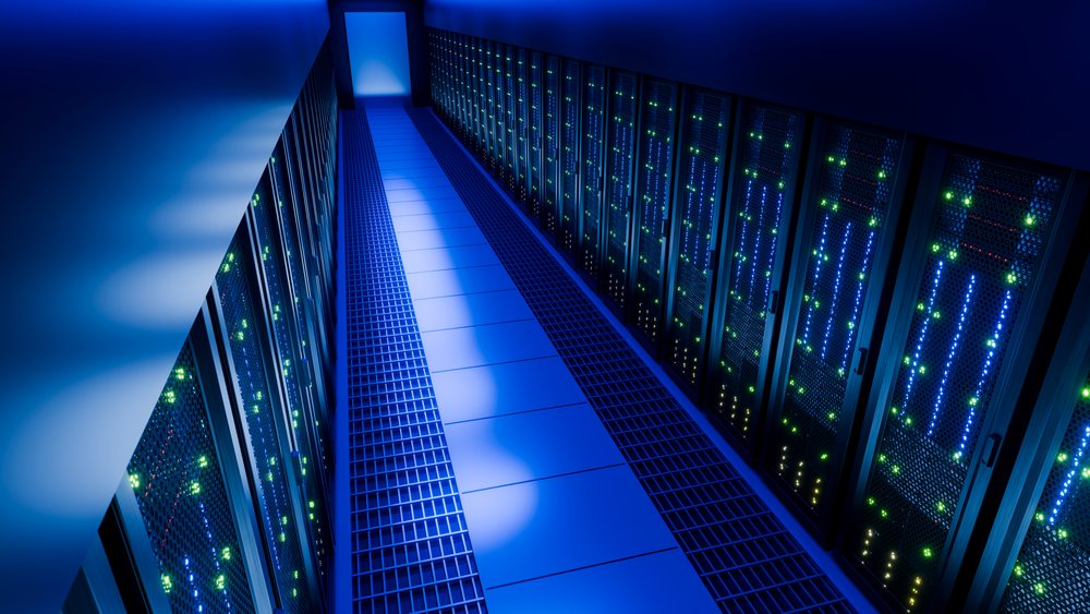 Data center corridor featuring multiple illuminated server racks and network equipment under blue LED lighting.