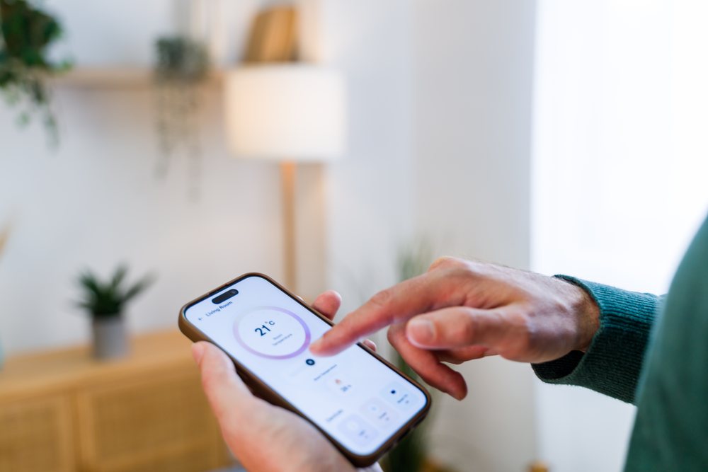 Person adjusting living room temperature to 21 degrees Celsius using a smartphone thermostat app indoors, Spain.