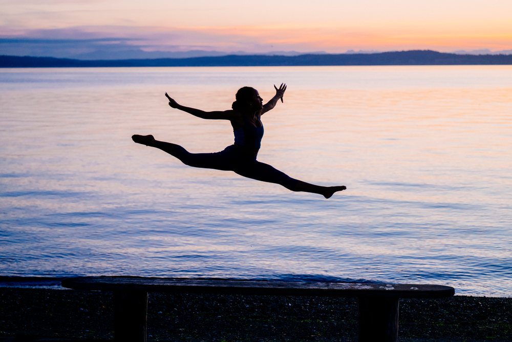 Silhouette of a woman performing a split jump at sunset over a calm lake, yoga, acrobatics, USA.