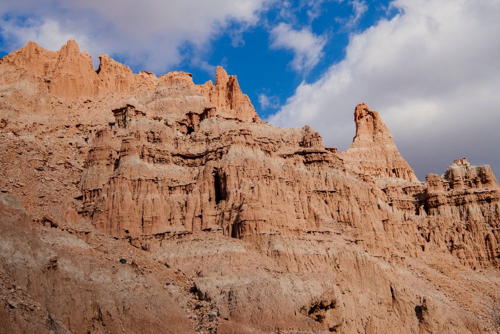 Cliffs and stratified red and tan sedimentary rock formations with natural spires at Cathedral Gorge State Park under a blue sky with clouds, Nevada, USA.
