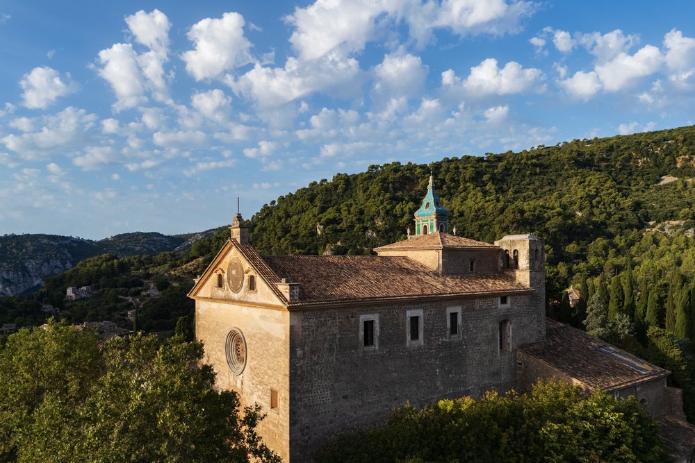 Sunrise illuminates a historic stone church with a blue-green dome and rose window, Landscape, Lifestyle, Valdemossa, Mallorca, Spain.