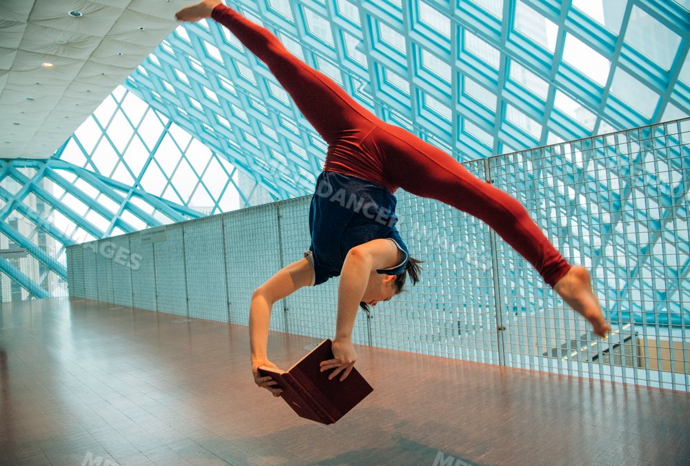 A woman performs a handstand holding a book