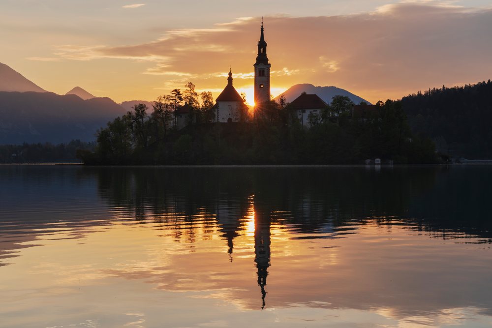 Church of the Assumption of the Virgin Mary on an island in Lake Bled at Sunrise with mountain reflections in the water, landscape, cityscape, Slovenia.