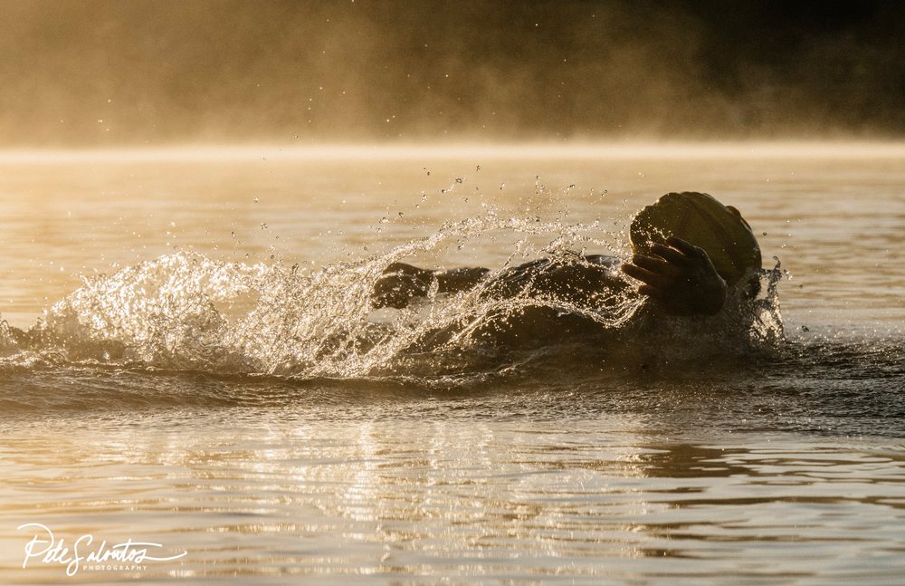Swimmer creating water splash while swimming in a lake during early morning mist, USA.