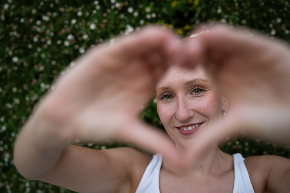A woman smiles while forming a heart shape with her hands outdoors, urban, Santiago De Compostela, Spain.
