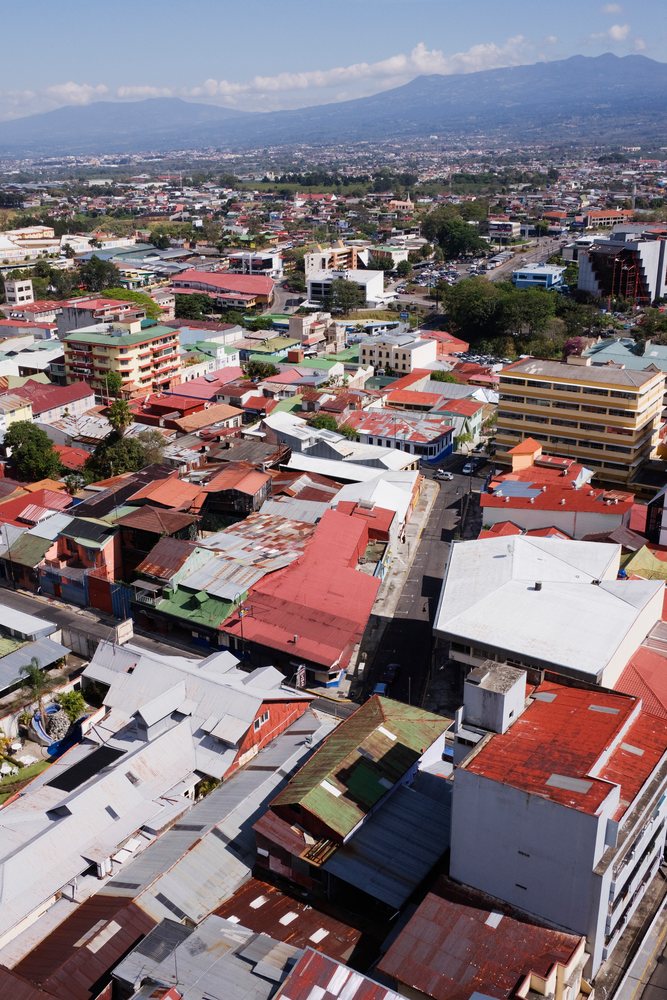 Aerial view of an urban and residential area, showing buildings, streets, and mountains under a clear sky, San Jose, Costa Rica.