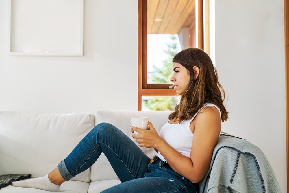 A young woman relaxes on a white sofa holding a cup