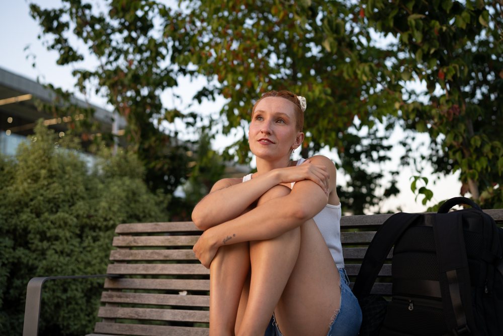 A young woman sits on a wooden bench outdoors, relaxing and reflecting near greenery, urban, Santiago De Compostela, Spain.