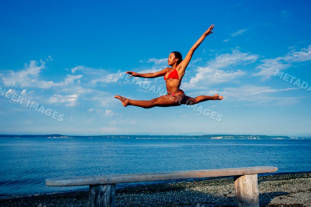 Woman jumping in a split over a bench on a beach in WA, USA