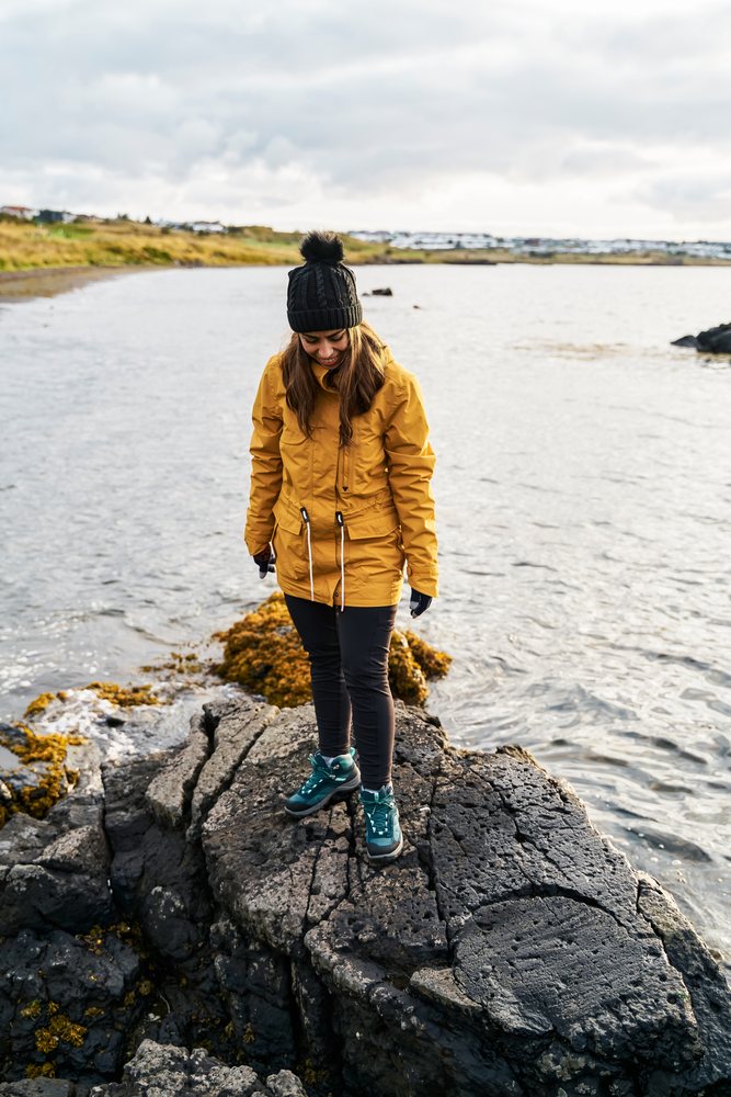 A white woman standing on volcanic rocks near the water in Iceland