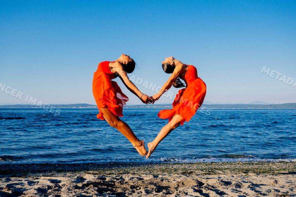 Two women jump holding hands performing partner acrobatics yoga