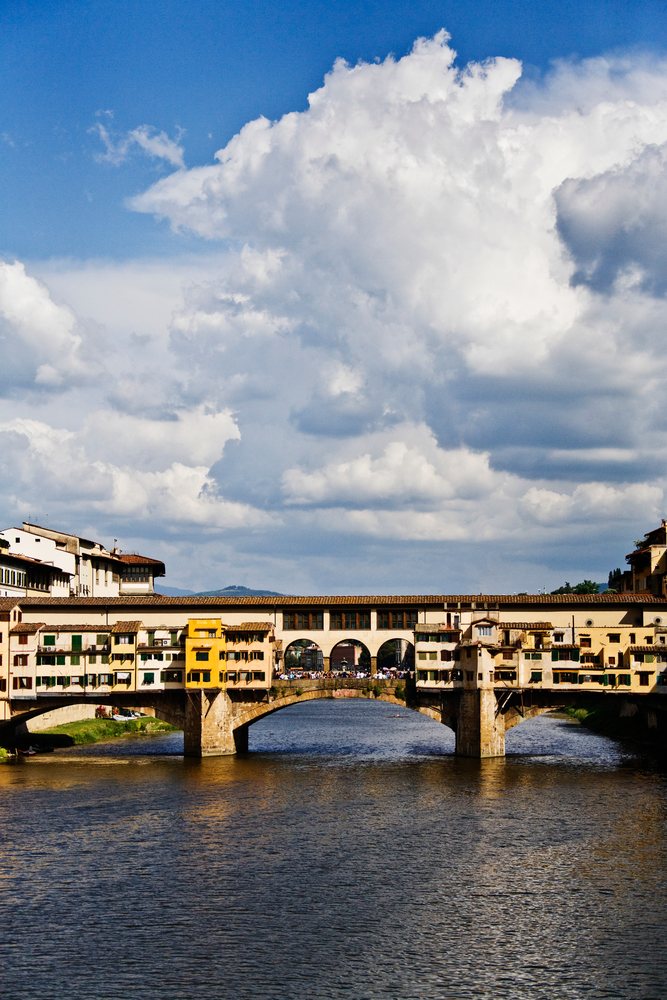 Historic Ponte Vecchio bridge with buildings arches reflecting over a river, Italy under a blue sky, Florence.