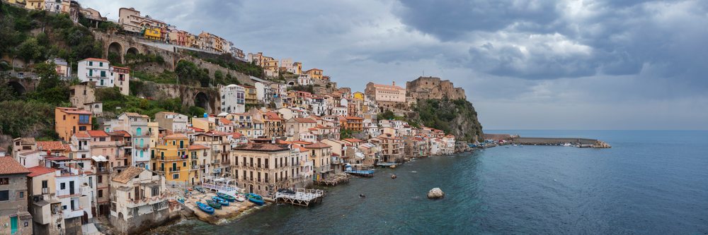 Coastal town of Chianalea in Calabria Italy with castle, harbor, and boats along the Mediterranean Sea under cloudy skies, Scilla.