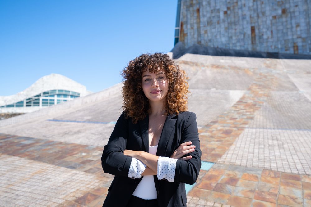 businesswoman with curly hair standing confidently with arms crossed outdoors by modern architecture in Santiago de Compostela, traveling executive, Spain, Antiago De Compostela.