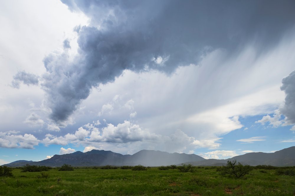 Storm clouds gather over Huachuca Peak with visible rainfall on green fields, Storm Chasing, Weather, Environment, Fort Huachuca, Arizona, USA.