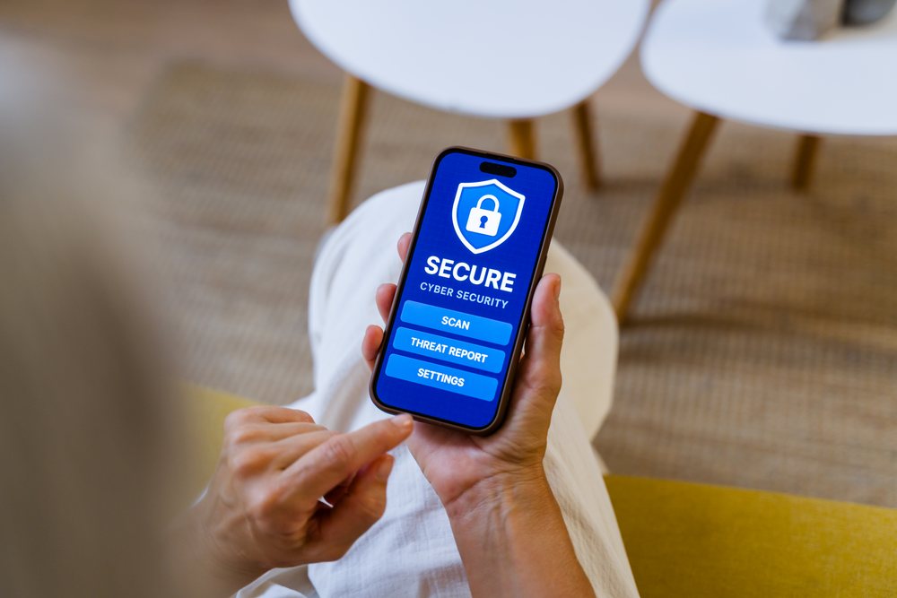 Person holding a smartphone indoors using a cyber security app with scan, threat report, and settings options visible on screen, Spain.