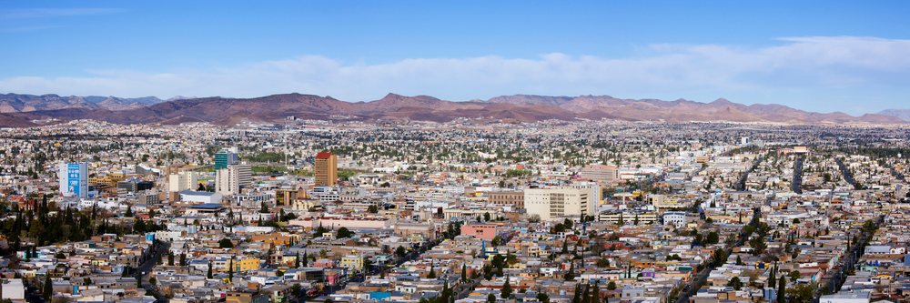 Urban cityscape of Chihuahua, showing buildings and a mountain range under blue sky with clouds, Mexico.
