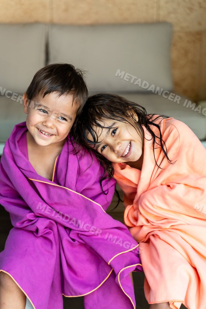 Two white children wrapped in towels smiling indoors in Madrid, Spain