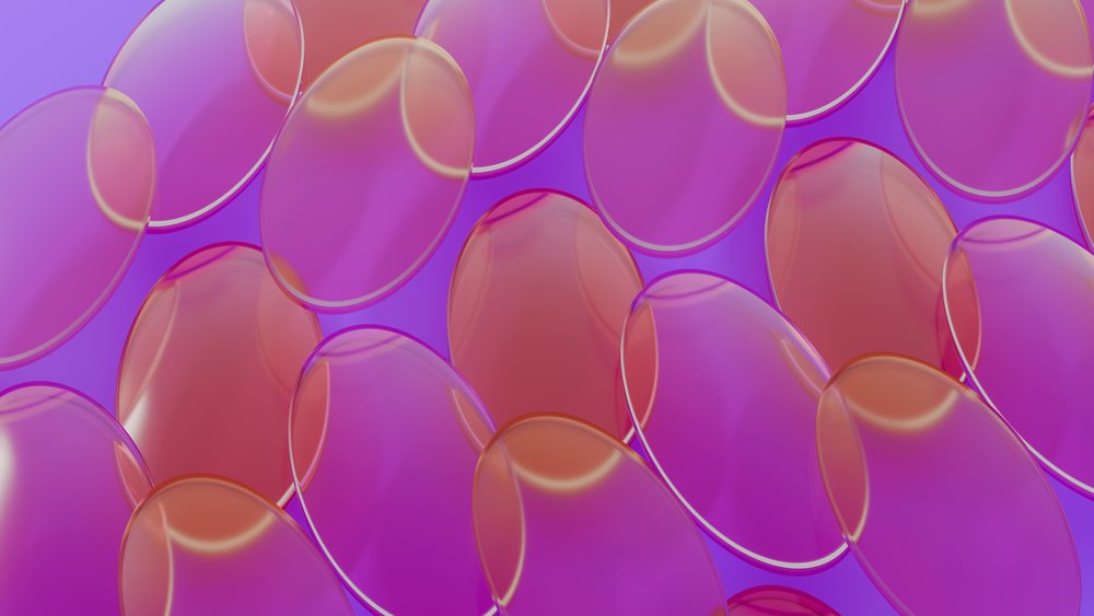 Closeup of multiple translucent orange and purple oval softgel capsules tightly packed with glossy surfaces.