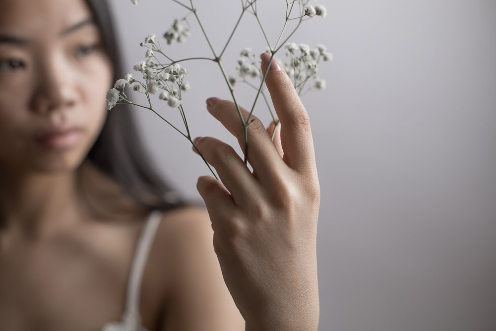 Woman gently holds delicate white flowers in a soft, emotional portrait close-up.