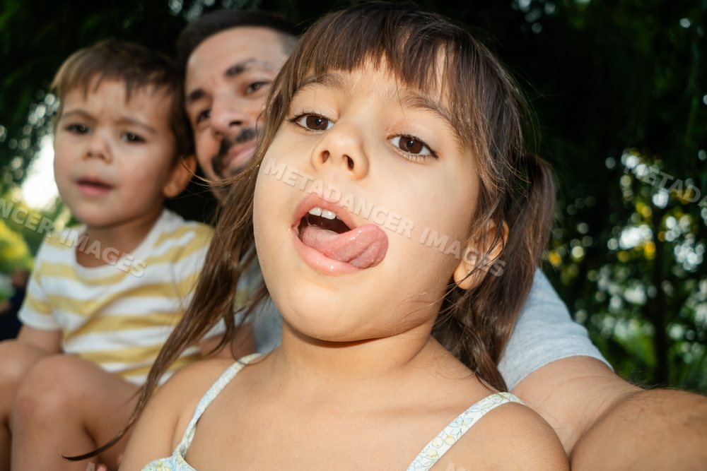 Young white girl sticks out tongue playfully with family outdoors