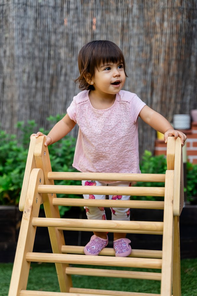 Toddler climbing a wooden play structure outdoors in a garden in Spain during daytime, kids.
