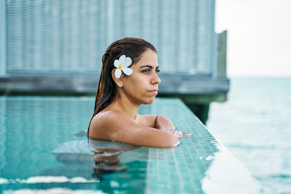 A white woman relaxing in a swimming pool with a flower in her hair