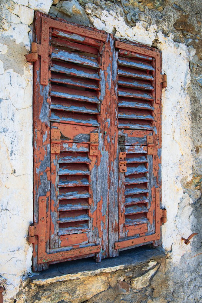Weathered wooden window shutters with peeling red and blue paint on a stone wall, Travel Photography, Castellare di Mercurio, Corsica, France.