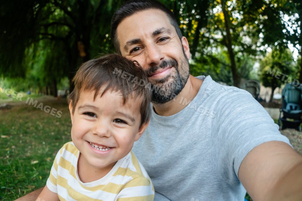 Father and son happily take a selfie together outdoors in a park
