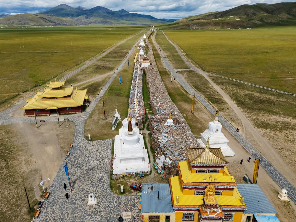 Aerial view showing the 1.6km Mani Wall with white Buddhist stupas and golden-roofed temples amid grasslands and mountains in Kham Tibet, Bagomah Mani Wall, Sichuan Province, People's Republic of China.