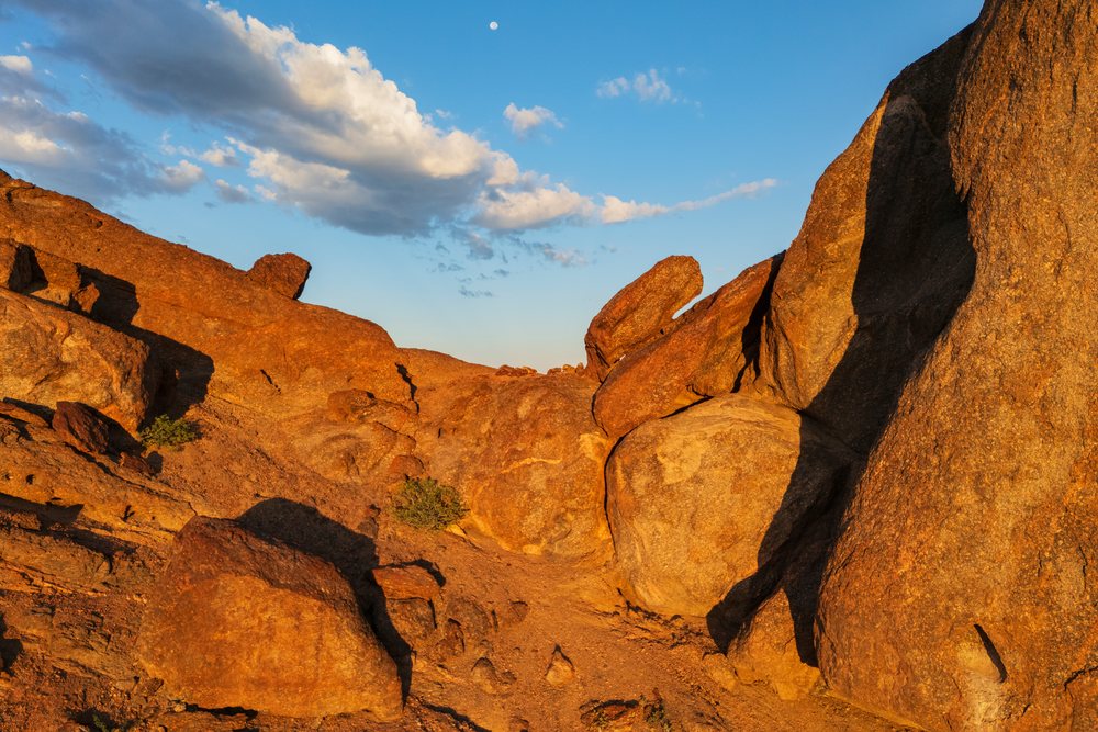 Granite rock formations and large boulders bathed in golden sunlight at The bear at Rock Gardens in Namibia's Kunene Region under a blue sky with clouds and the moon, landscape, wildlife.