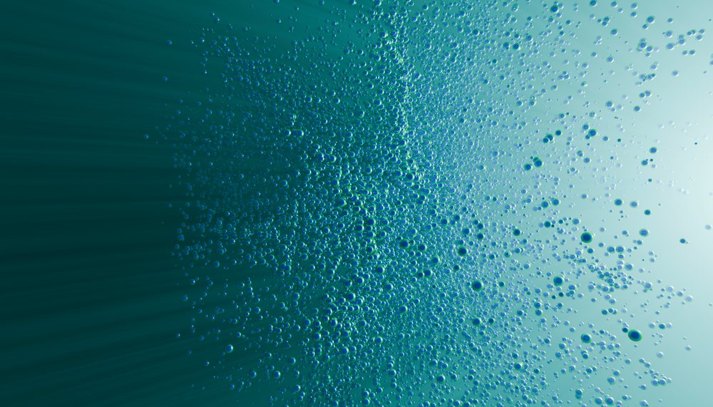 Bubbles rising and clustering in clear blue water with light rays shining through the liquid.